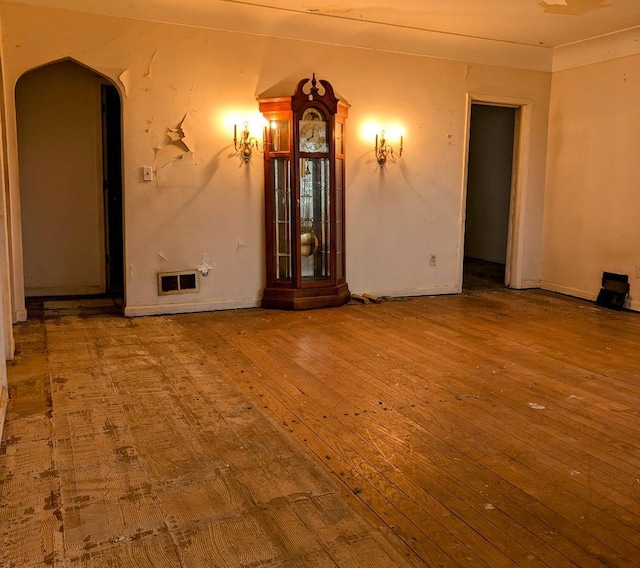 unfurnished room with arched walkways, visible vents, and hardwood / wood-style flooring