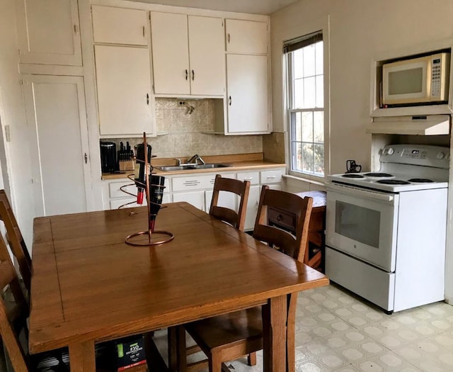 kitchen with a sink, white appliances, light floors, and white cabinets