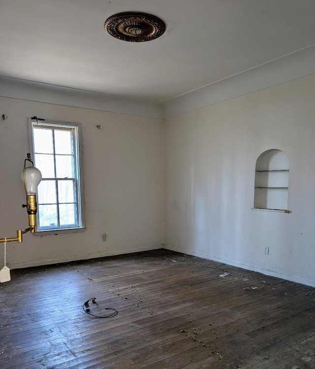 spare room with dark wood finished floors, built in shelves, and baseboards