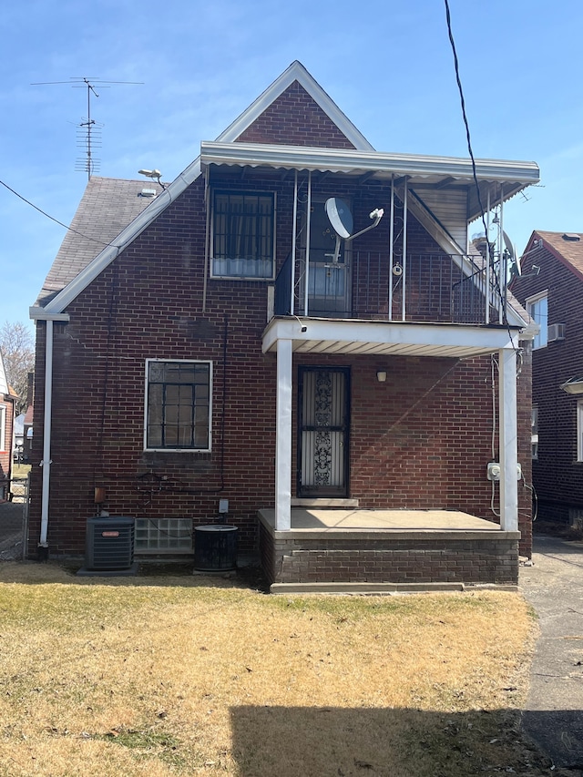 view of front of property featuring central air condition unit, brick siding, a balcony, and a front lawn