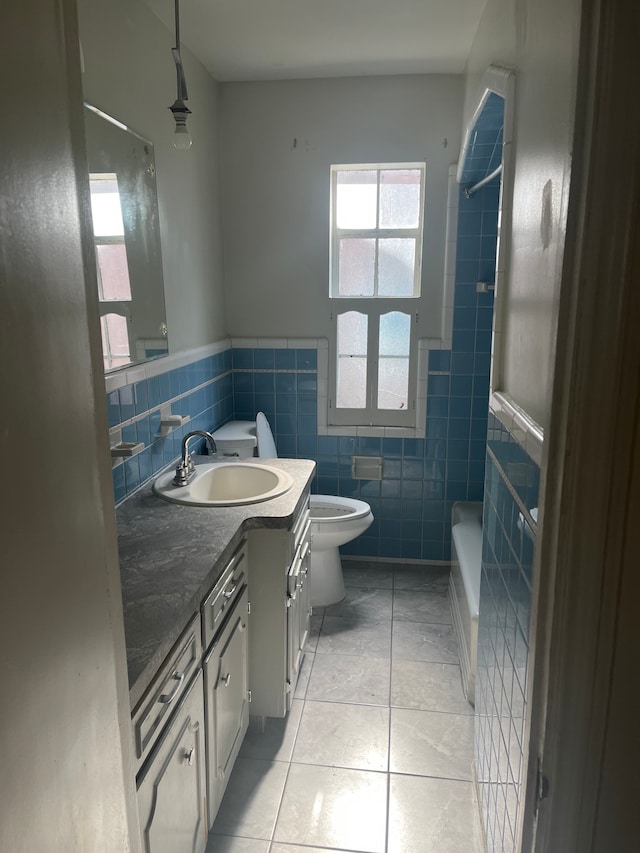 bathroom with washtub / shower combination, toilet, vanity, tile patterned floors, and tile walls