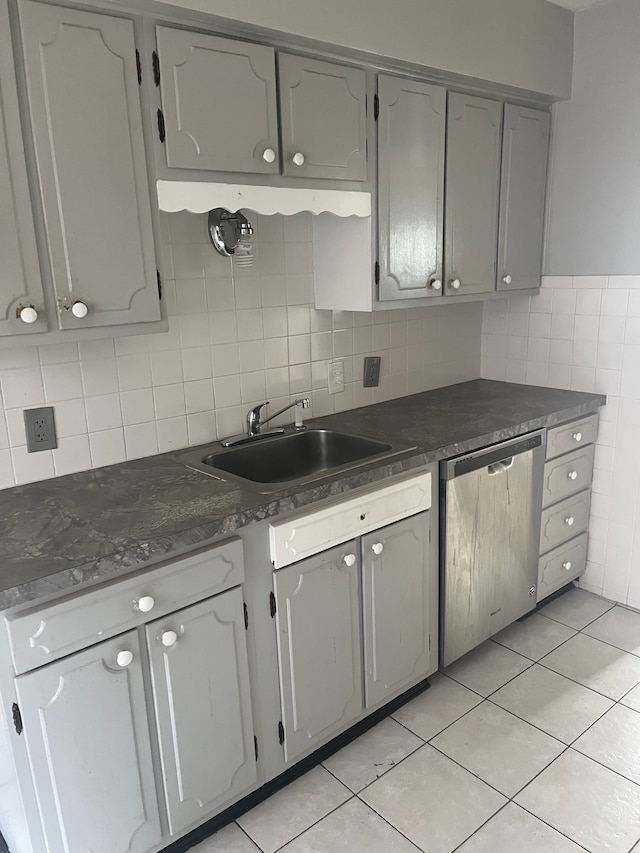 kitchen with a sink, stainless steel dishwasher, dark countertops, and light tile patterned floors