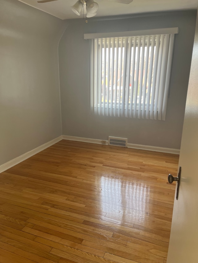 empty room with wood finished floors, a ceiling fan, visible vents, and baseboards