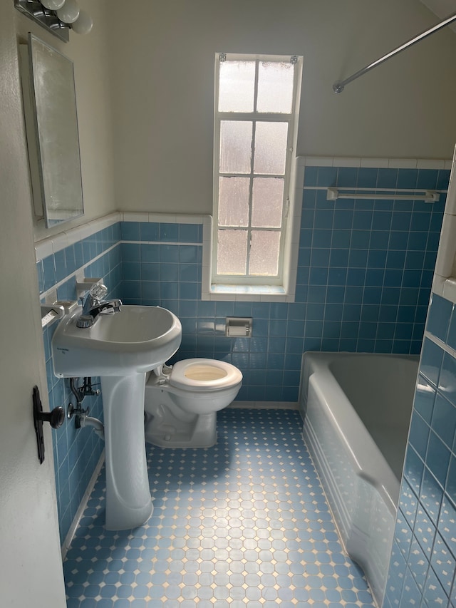 bathroom with a wainscoted wall, toilet, tile walls, and a bath