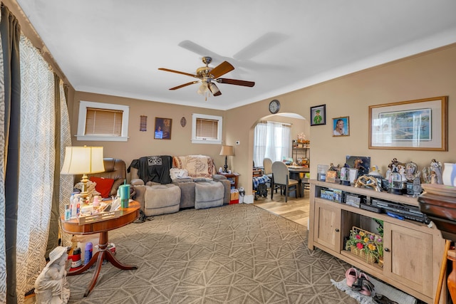 living area featuring arched walkways, ornamental molding, and a ceiling fan