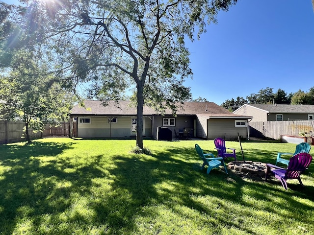 rear view of property featuring a lawn, a fenced backyard, and an outdoor fire pit