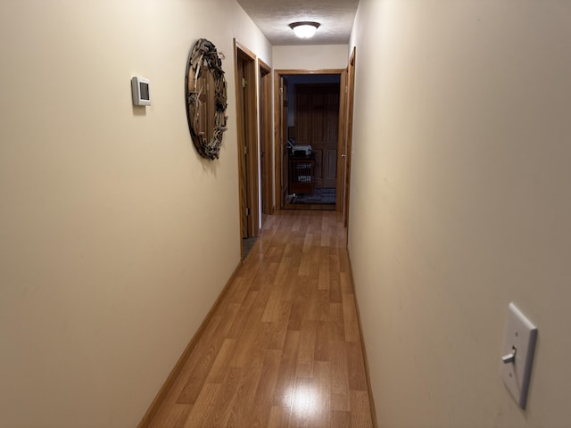 hallway with light wood-type flooring, baseboards, and a textured ceiling