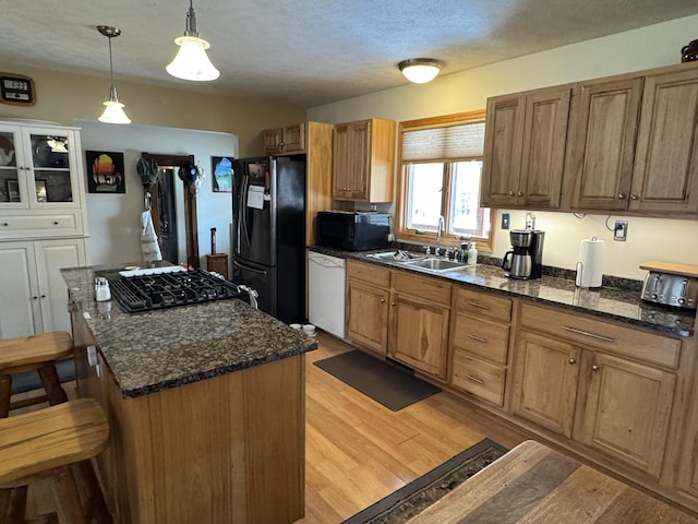 kitchen with a kitchen bar, black appliances, light wood-style flooring, a sink, and a center island