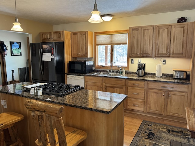 kitchen featuring black appliances, a sink, decorative light fixtures, a kitchen breakfast bar, and light wood finished floors