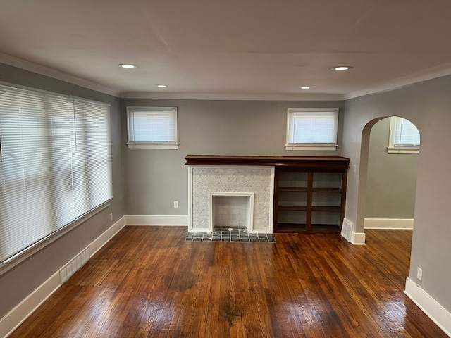 unfurnished living room with dark wood-style floors, visible vents, baseboards, a fireplace, and arched walkways