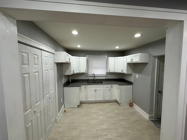 kitchen with dark countertops, recessed lighting, white cabinetry, and a sink