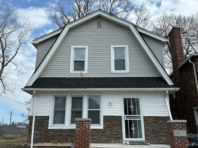 view of front of home featuring stone siding, a gambrel roof, and a shingled roof