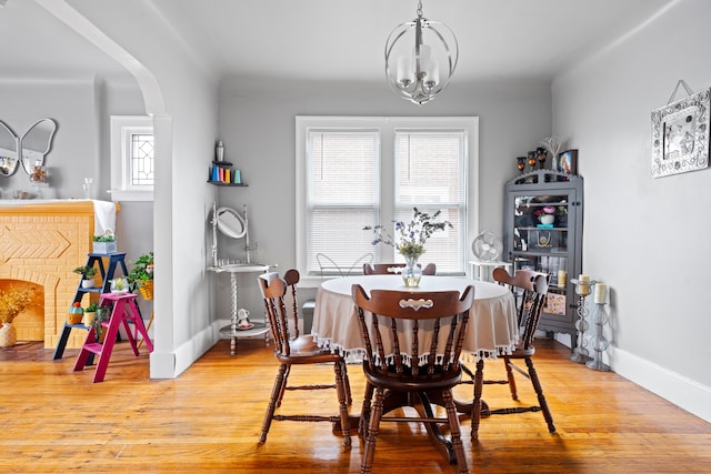 dining room with light wood-type flooring, arched walkways, a notable chandelier, and baseboards