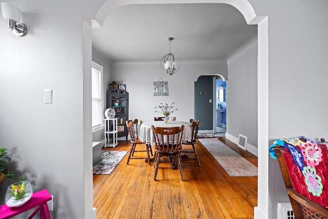 dining area featuring arched walkways, visible vents, baseboards, and wood finished floors