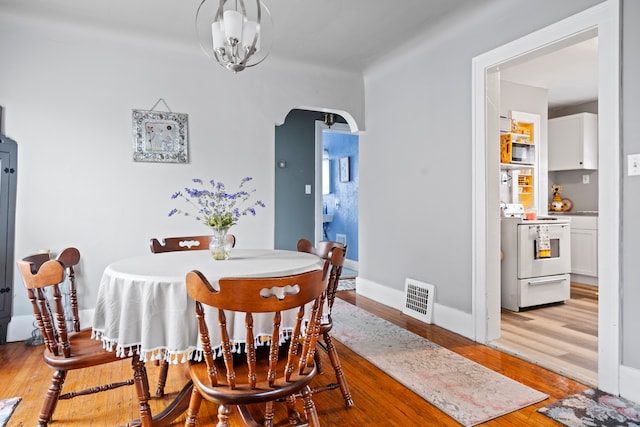 dining room with arched walkways, visible vents, light wood-style flooring, and baseboards