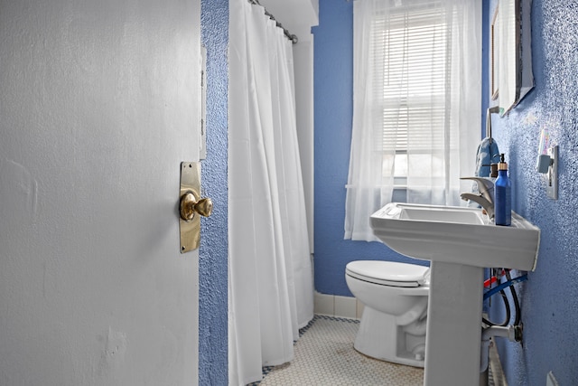 bathroom with tile patterned floors, a shower with curtain, toilet, and a textured wall