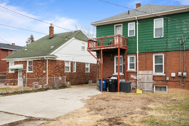 rear view of property featuring central AC, concrete driveway, a balcony, and fence