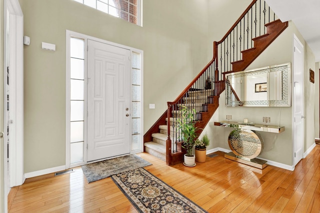 entrance foyer with stairway, baseboards, visible vents, a high ceiling, and wood-type flooring