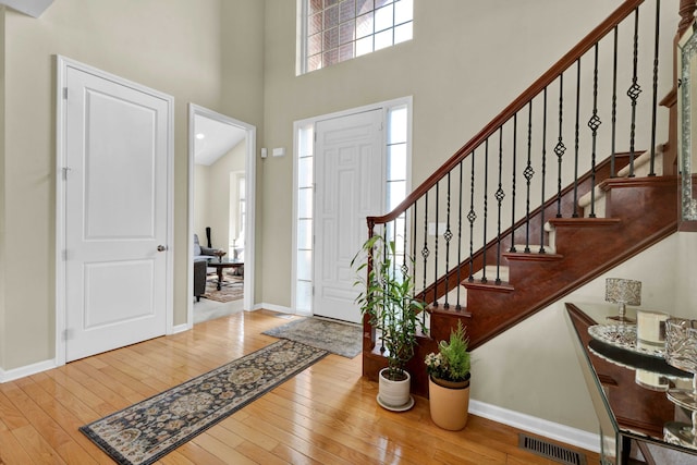 foyer entrance featuring baseboards, visible vents, a high ceiling, stairs, and hardwood / wood-style flooring