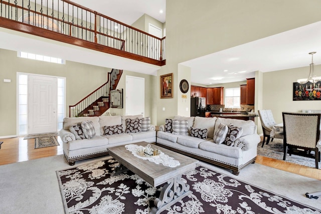 living area featuring a chandelier, light wood-type flooring, stairs, and a towering ceiling