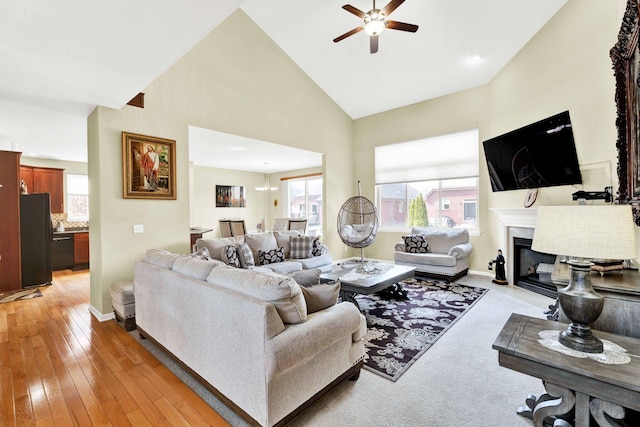 living area featuring baseboards, ceiling fan, a fireplace with flush hearth, light wood-type flooring, and high vaulted ceiling