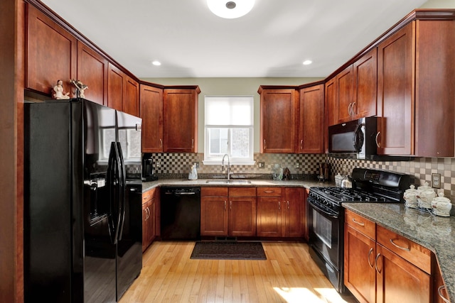 kitchen featuring tasteful backsplash, light wood finished floors, dark stone counters, black appliances, and a sink