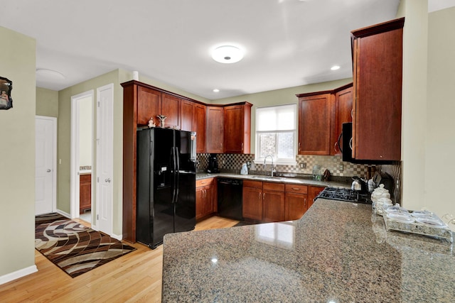 kitchen featuring baseboards, light wood-type flooring, decorative backsplash, black appliances, and a sink