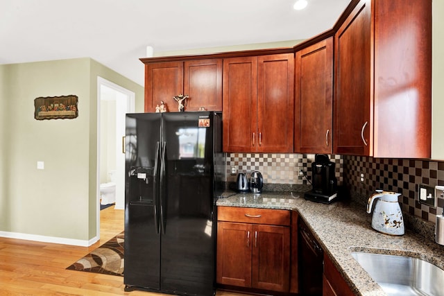 kitchen with backsplash, light wood-style floors, stone countertops, black appliances, and a sink