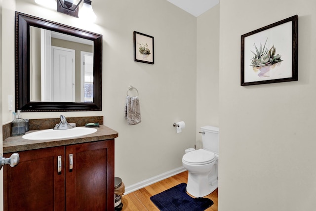 bathroom featuring baseboards, toilet, wood finished floors, and vanity