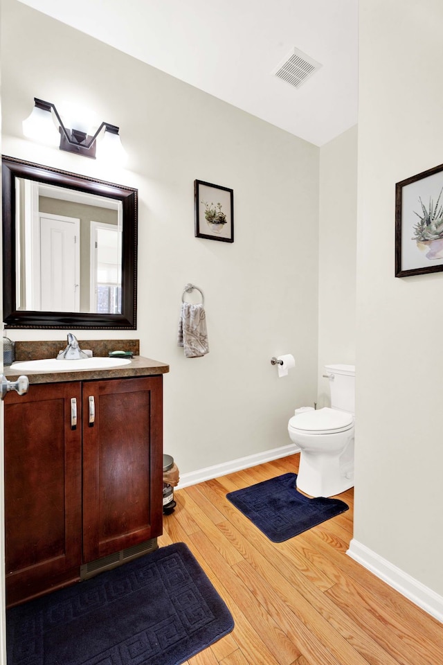 half bathroom with visible vents, baseboards, toilet, wood finished floors, and vanity