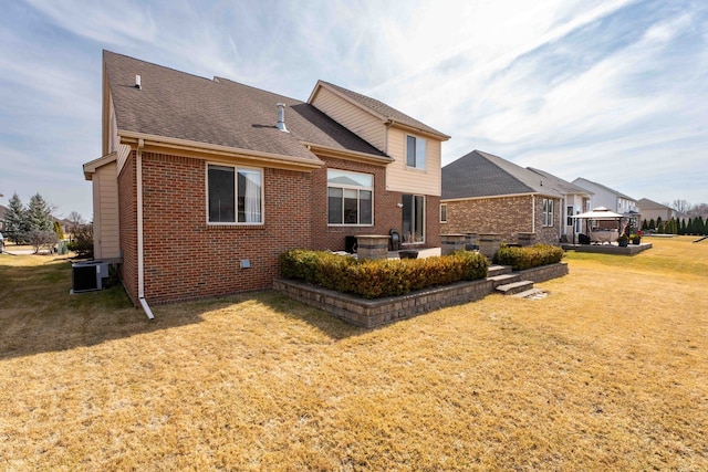 rear view of property with central air condition unit, a lawn, roof with shingles, brick siding, and a patio area