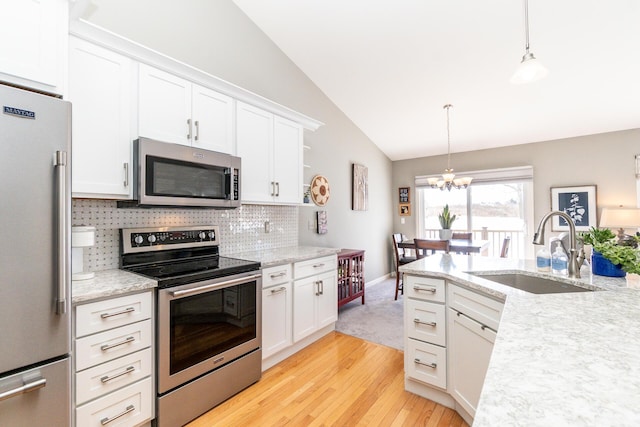 kitchen with a sink, stainless steel appliances, vaulted ceiling, white cabinetry, and a notable chandelier