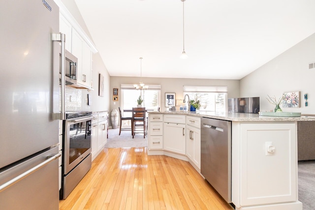 kitchen with light wood-type flooring, stainless steel appliances, white cabinets, and decorative light fixtures