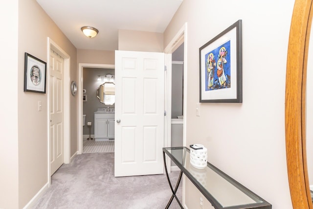 hall featuring light colored carpet and baseboards