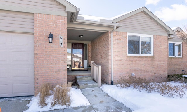 snow covered property entrance featuring brick siding and a garage