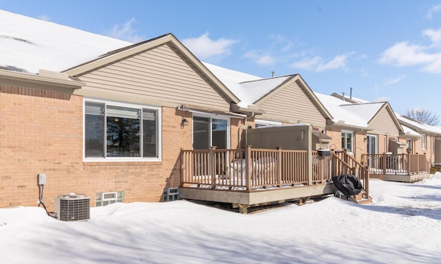 snow covered back of property with brick siding, cooling unit, and a wooden deck