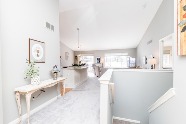 corridor with visible vents, light carpet, high vaulted ceiling, and an upstairs landing