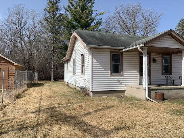 view of front of home with covered porch, a shingled roof, a front yard, and fence