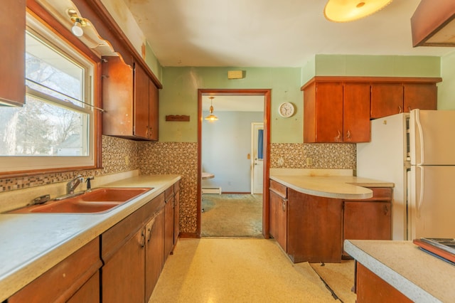 kitchen with a sink, light countertops, freestanding refrigerator, brown cabinetry, and a baseboard radiator