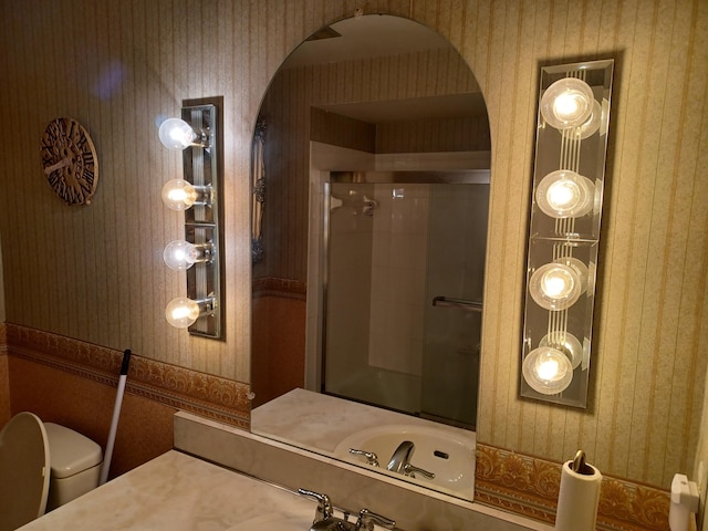 bathroom featuring a shower stall, wallpapered walls, toilet, and a sink