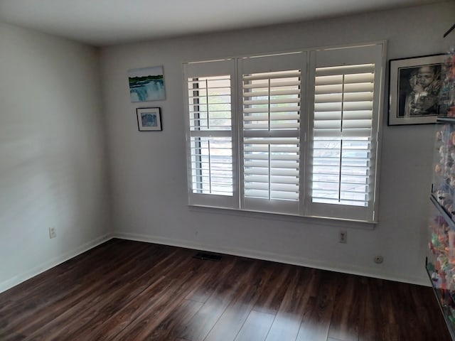 spare room with dark wood finished floors, a healthy amount of sunlight, visible vents, and baseboards