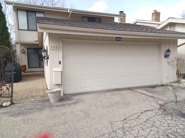 view of front of house with driveway, an attached garage, and a shingled roof