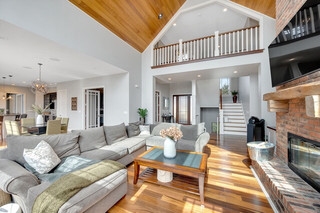 living room with a fireplace, stairway, high vaulted ceiling, an inviting chandelier, and hardwood / wood-style floors