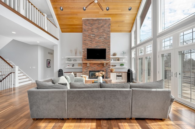 living area with stairs, a brick fireplace, wood finished floors, high vaulted ceiling, and wood ceiling