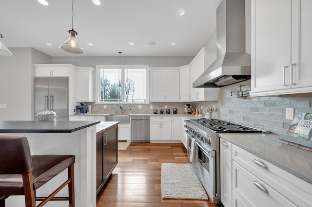 kitchen featuring white cabinets, a sink, a kitchen breakfast bar, wall chimney exhaust hood, and premium appliances