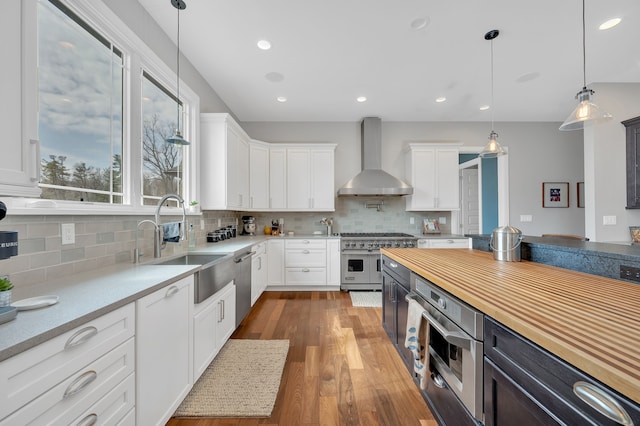 kitchen featuring a sink, appliances with stainless steel finishes, white cabinets, and wall chimney range hood