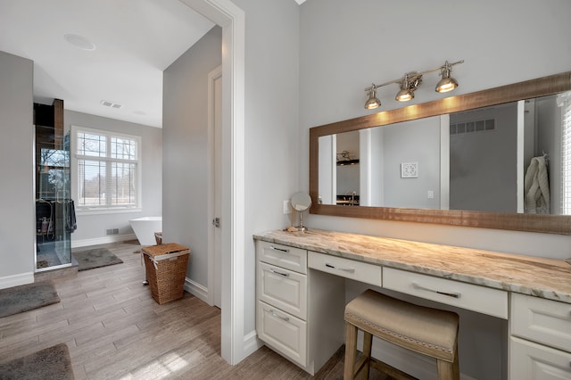 full bath featuring visible vents, vanity, a freestanding bath, and wood finished floors