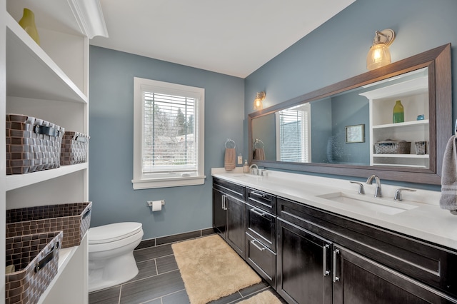 bathroom with double vanity, toilet, baseboards, and a sink