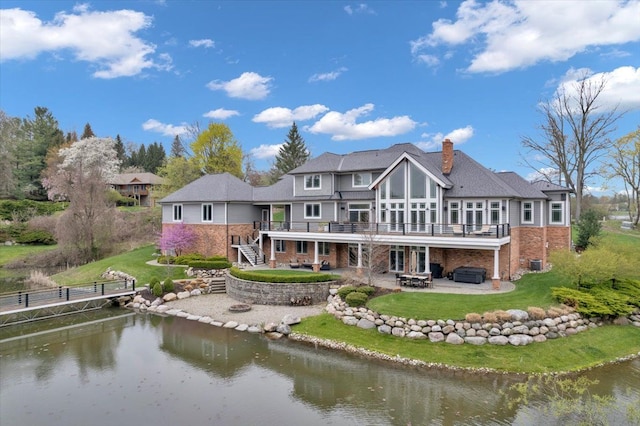 back of property with a deck with water view, a patio area, stairway, a hot tub, and a fire pit