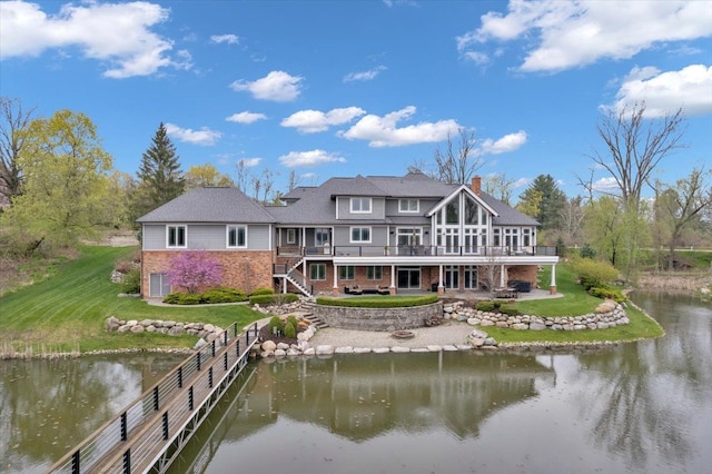 rear view of house featuring stairs, a yard, a deck with water view, and brick siding